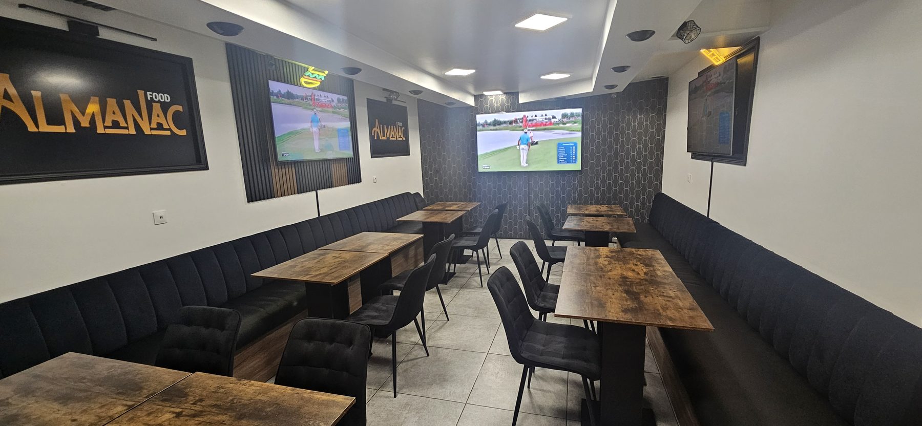 La salle à l'arrière du restaurant Almanac Food : banquettes en velours, grandes tablées et écrans diffusant du sport